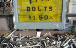Bin of mixed nuts and bolts with a yellow sign above it reading bolts $1.50.