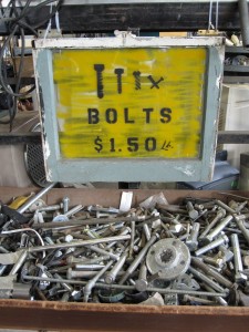 Bin of mixed nuts and bolts with a yellow sign above it reading bolts $1.50.